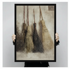 Antique straw brooms oil painting in black frame held in hands, product mockup showing witchy cottagecore wall art print size and premium frame quality