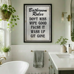 Framed vintage Bathroom Rules funny quote canvas wall art with bold black distressed typography on white textured background hung in a bright bathroom with freestanding bathtub gold hardware and hanging plants