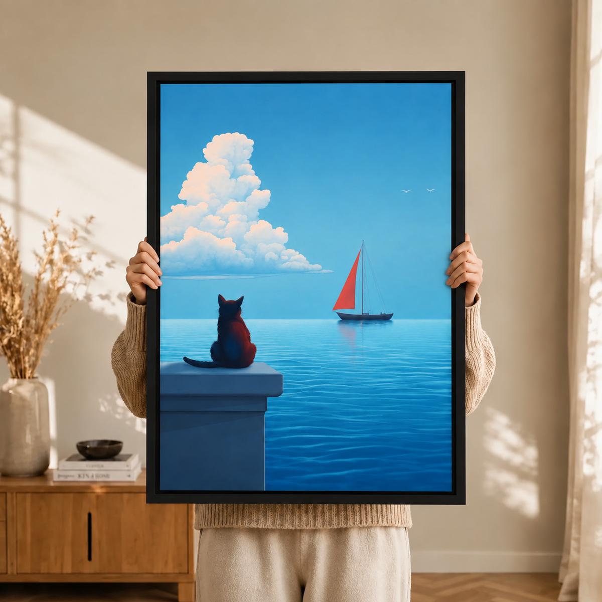 Close-up of a black-framed wall art print showing a black cat perched on a ledge gazing at a red sailboat across a tranquil blue sea