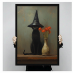 Hand-held framed wall art print showing a black cat wearing a pointed witch hat seated next to a cream vase with red flowers on a wooden shelf