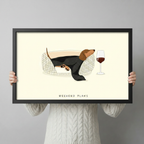 Person holding a black framed art print of a dachshund resting in a basket with a red wine glass, cream background with Weekend Plans text