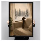 Hand-held framed canvas art print showing a dachshund on a sofa watching snowflakes fall over pine trees through sheer curtains