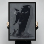 Hand-held display of a black-framed canvas art print featuring a dramatic dark gothic skeleton emerging from a coffin with a raven on its skull, reaching toward a small animal among wildflowers on a charcoal grey background