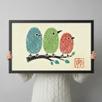 Person in a cream knit sweater holding a large horizontal black framed fingerprint birds on a branch canvas art print with three round teal green and red fingerprint-textured birds perched on a black ink branch with teal leaves on a warm cream background