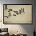 Black framed vintage Canada geese flying in formation canvas wall art with aged parchment background displayed in a modern dark gray living room with gray sofa, candlestick holders and tall black vase