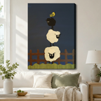Stretched canvas wall art of a charming folk art stacked sheep and yellow bird print featuring two plump cream woolly sheep stacked vertically with a small round black sheep on top and a cheerful yellow bird perched on its back above a rustic brown picket fence and a wavy green meadow strip on a deep navy blue background, hung above a white sofa with sage green and cream pillows and a white ceramic table lamp in a bright airy living room