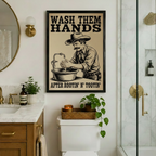 Framed funny cowboy "Wash Them Hands" canvas art hung above a toilet in a marble and gold luxury bathroom, blending rustic western humor with an upscale interior