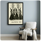 Black framed witchcraft wall art print showing four women in long dark dresses and witch hats among leafless trees with Girls Will Be Girls caption, styled beside a white linen armchair on a blue-grey wall
