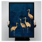 Person holding a large black framed gold foil crane quartet canvas art print showing print size scale and detailed golden crane silhouette texture on a deep navy blue abstract brushstroke background