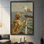 Black framed coastal vintage oil painting of a fluffy golden retriever standing on its hind legs with front paws on a wooden boat railing gazing up at a white and gray seagull perched on the post with a blue-gray ocean and cloudy sky in the background animal canvas wall art displayed in a modern gray living room with dark sofa and metal candlesticks