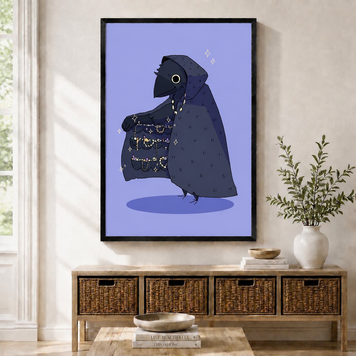 Black-framed gothic crow wall art print featuring a hooded raven displaying a sparkling treasure cloak, hung above a wicker storage console in a Scandinavian entryway
