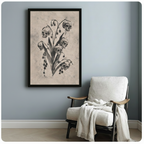 Black framed gothic skull botanical canvas art print with five human skulls on a lily of the valley stem and dark hanging berries in vintage charcoal illustration style on aged beige background beside a white linen armchair