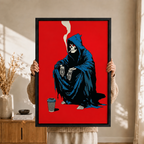 Person holding a black-framed graphic wall art canvas featuring a dark humor grim reaper skeleton in a blue robe smoking and sitting beside a coffee cup against a striking red background, bohemian interior setting