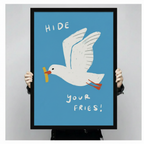 "Hide Your Fries" seagull illustrated framed print held up to show full size, bold blue background with white bird and yellow chip detail