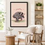 Black framed Jimothy opossum illustration print with pink heart accents mounted on a white wall above a linen armchair in a Scandinavian-style reading corner with natural wood side table