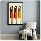 Black framed mid-century modern three abstract birds with round eyes art print in orange and teal on a light blue-grey wall beside a white linen armchair with draped throw