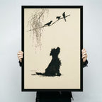 Person holding a black framed minimalist ink-style terrier dog silhouette gazing at three birds on willow branch art print on cream background against a light gray backdrop
