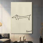 Picasso-inspired minimalist continuous line dachshund silhouette with handwritten signature gallery wrap canvas art on warm cream background displayed on a dark gray paneled wall above a charcoal sofa with brass candle holders