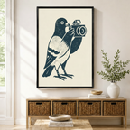 Framed navy blue linocut-style pigeon holding a vintage camera on cream background wall art displayed above a wicker storage console in a bright modern entryway