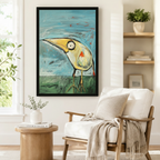 Black framed whimsical big beak bird wall art print on teal and green background beside white linen accent chair and round side table in Scandinavian reading nook