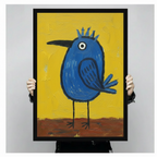Close-up of a black framed art print showing a bold round blue bird with a spiky crown, single white eye, and thin black legs on a vivid yellow and brown textured background, held up by two hands
