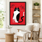 Black framed retro folk art black and white tuxedo cat canvas art showing a stoic cat seated upright with two small sketched birds hovering above on a vivid red distressed background, displayed on a white wall beside a white wooden armchair with a cream fringed throw and a round wood side table with books