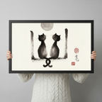 Person in white sweater holding large framed Chinese ink wash print of two cats facing each other under a full moon — size reference lifestyle photo