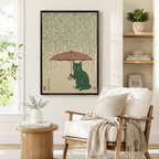 Vintage Japanese-inspired framed print of a black cat holding an umbrella in the rain, displayed in a cozy reading nook with a linen armchair and natural wood side table