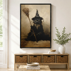 Framed gothic wall art print of a brooding black cat wearing a witch hat and holding a broomstick in a vintage oil painting style, displayed above a wicker storage console in a bright entryway